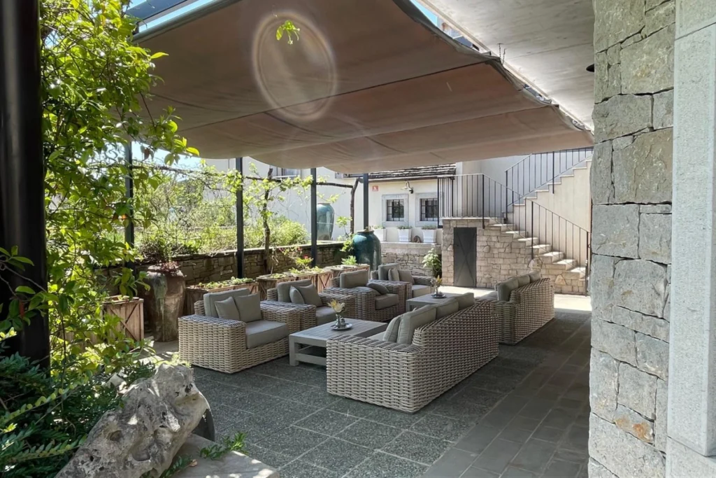 15 Ý Tưởng Decor Ban Công Đẹp Cho Cuộc Sống Thêm Chill 14 Không gian ban công phong cách tối giản với sofa mây tre, bàn nhỏ, mái che và nhiều cây xanh tạo cảm giác thoải mái và hài hòa.