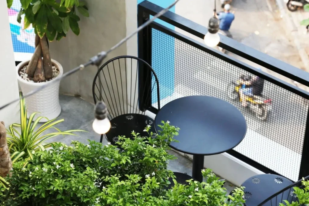 15 Ý Tưởng Decor Ban Công Đẹp Cho Cuộc Sống Thêm Chill 9 Bàn tròn nhỏ màu đen đặt ngoài ban công, kết hợp ghế ngồi, đèn bàn và cây xanh tạo góc làm việc đơn giản, hiện đại.