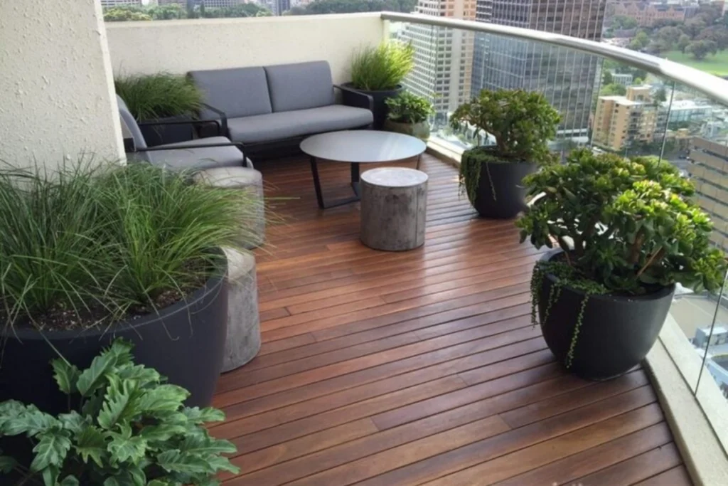 15 Ý Tưởng Decor Ban Công Đẹp Cho Cuộc Sống Thêm Chill 11 Ban công với sofa đệm, bàn tròn nhỏ, chậu cây xanh và sàn gỗ ngoài trời mang đến không gian thư giãn ấm áp và sang trọng.