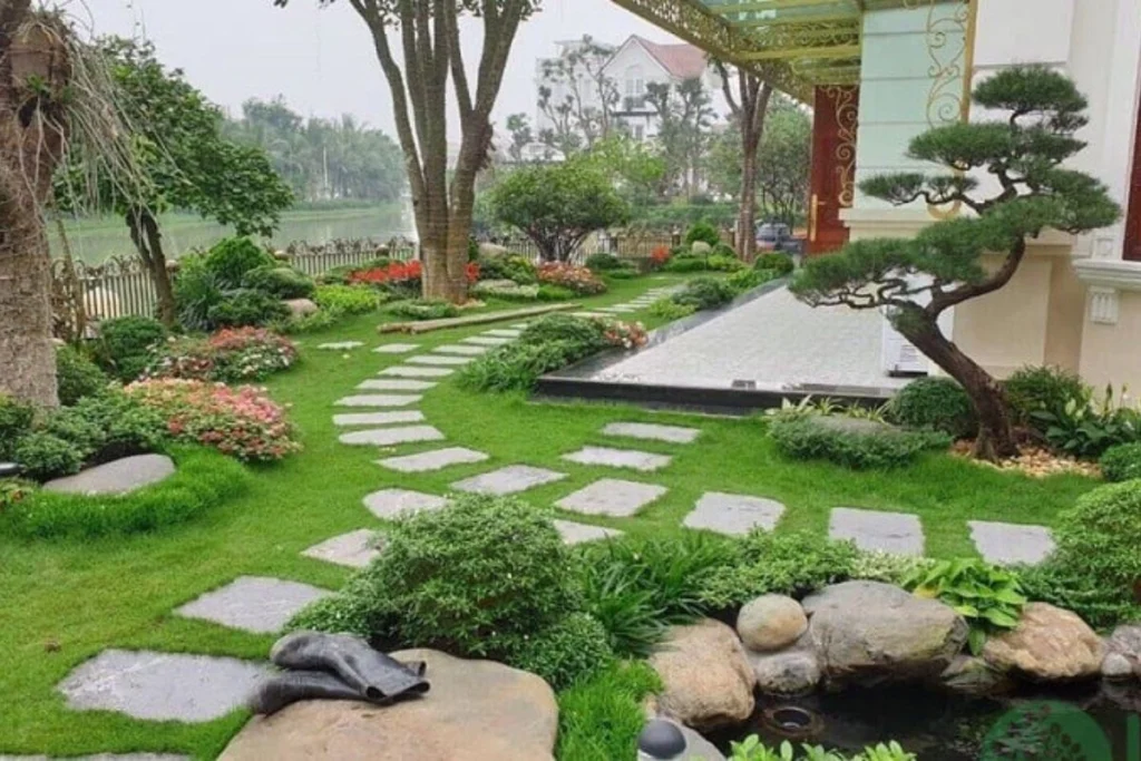 đồi cỏ xanh, đá lát tạo lối đi, cây cảnh xung quanh, bờ sông
