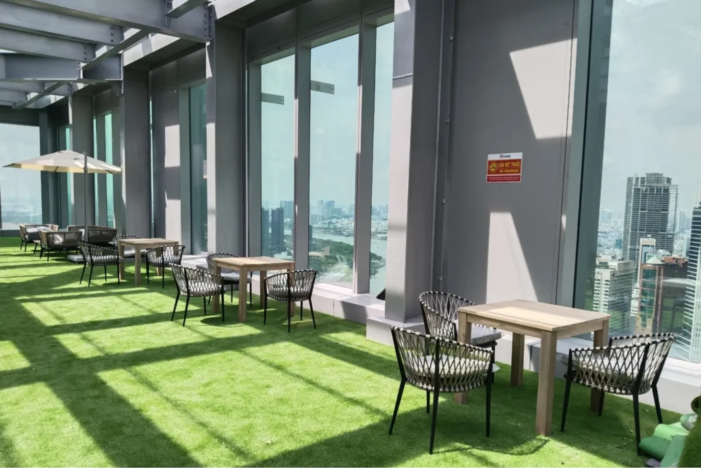 Không gian rooftop café với bàn ghế ngoài trời hiện đại, tầm nhìn toàn cảnh thành phố, tạo cảm giác thoáng đãng và thư giãn.  