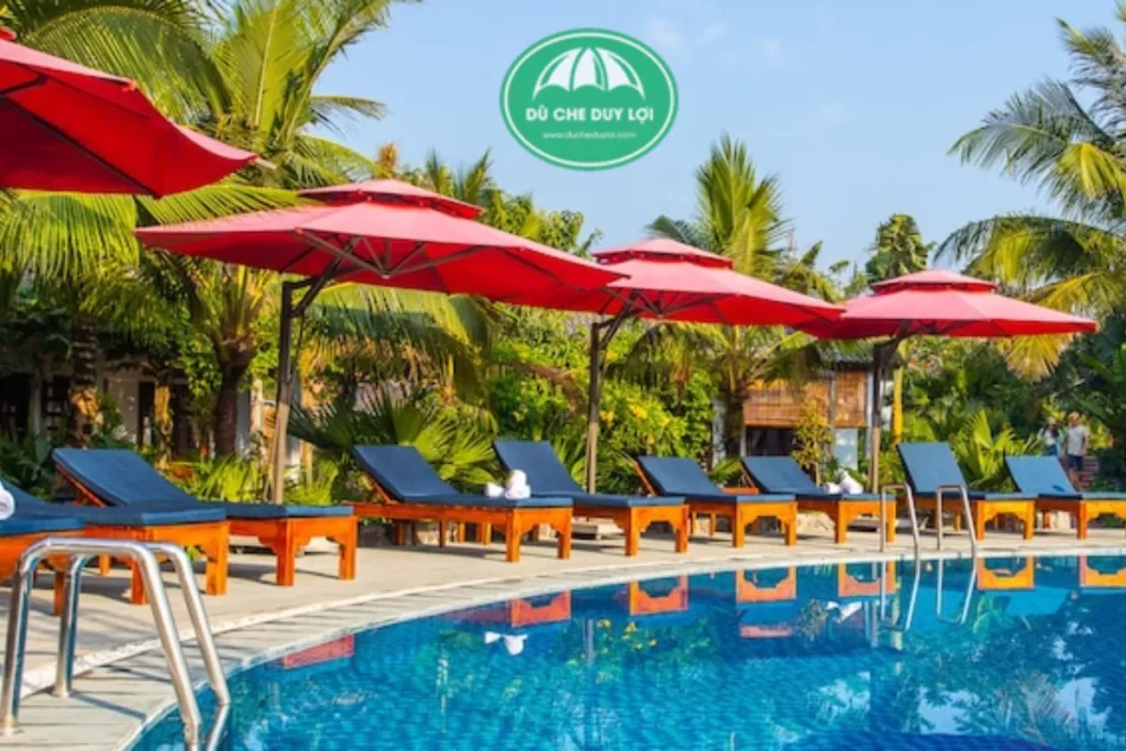 Top công ty bán dù che nắng uy tín 2025 bạn nên biết 7 Dù che nắng Duy Lợi tại khu nghỉ dưỡng, tán dù đỏ nổi bật giữa hàng dừa xanh, tạo bóng mát cho khu hồ bơi.