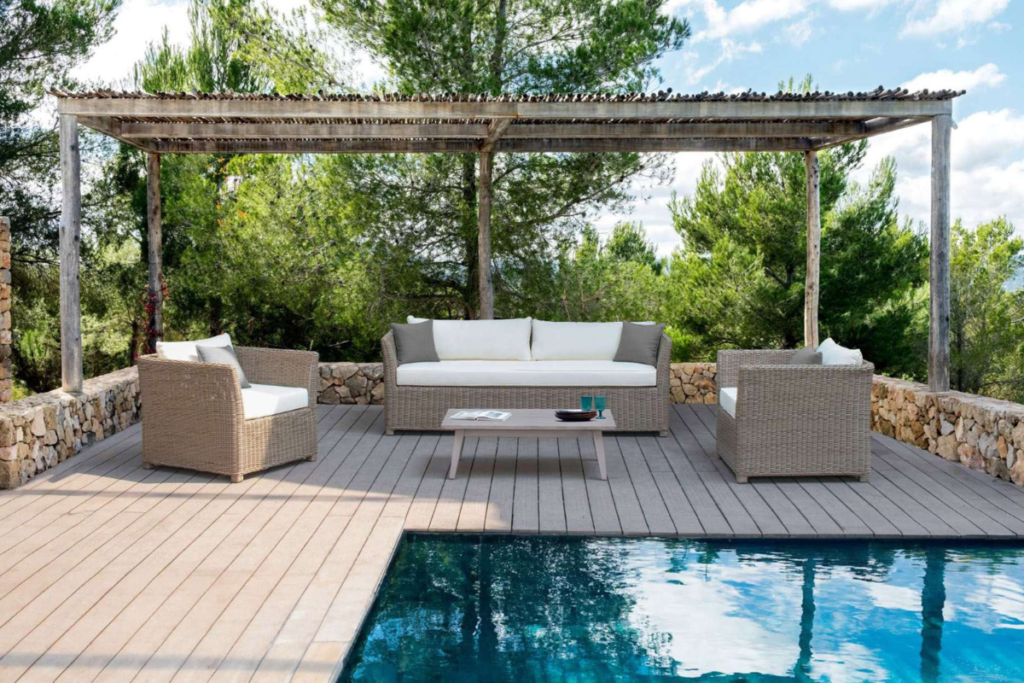 Bộ sofa mây nhựa đặt dưới giàn pergola cạnh hồ bơi, kết hợp đệm sáng màu tạo cảm giác thư giãn và hài hòa với thiên nhiên