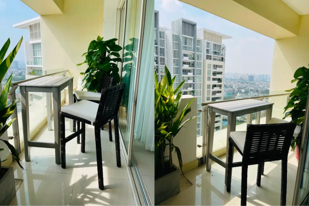 Bộ ghế quầy bar đặt trên ban công căn hộ hiện đại, gồm bàn cao và ghế mây nhựa, bố trí cạnh cửa kính với cây xanh và view thành phố.