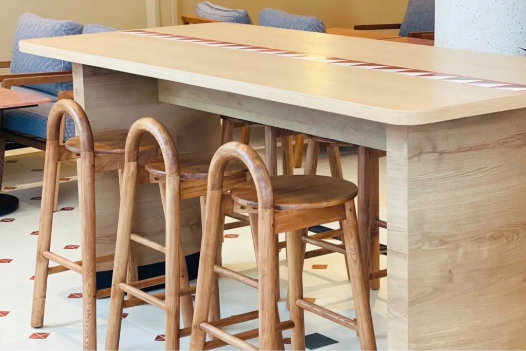 Ghế quầy bar phong cách Scandinavian bằng gỗ sáng màu, thiết kế bo tròn, đặt dọc theo quầy bar gỗ trong không gian nội thất sáng.