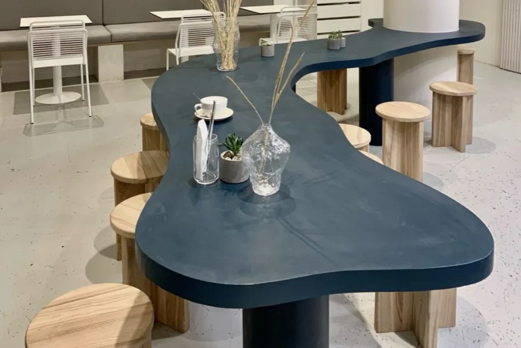 Mẫu bàn xi măng màu xanh đậm uốn lượn kết hợp với ghế gỗ nhỏ trong quán cafe phong cách tối giản. 